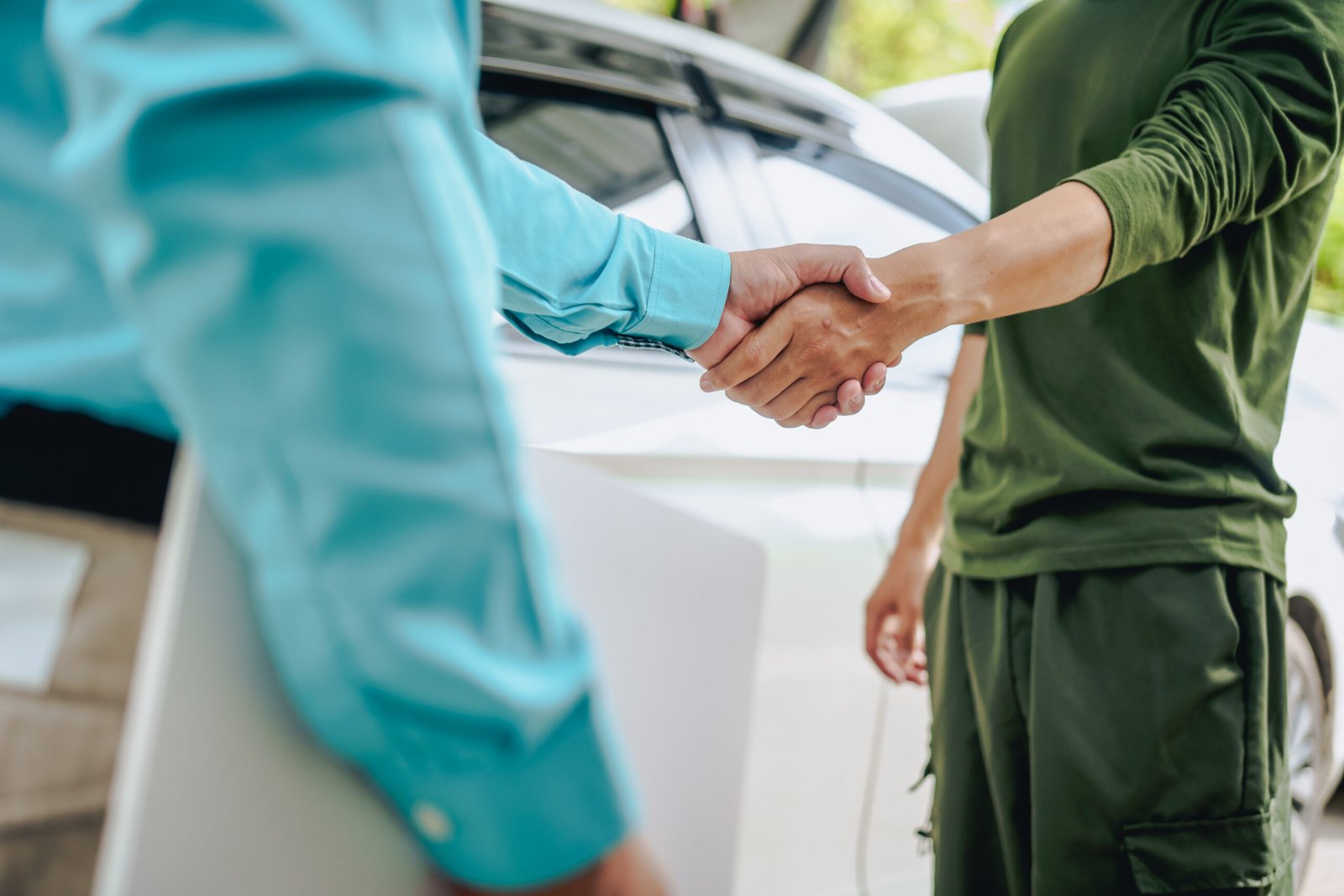 Poignée de main entre deux personnes devant une voiture, symbole de confiance et d’accord.