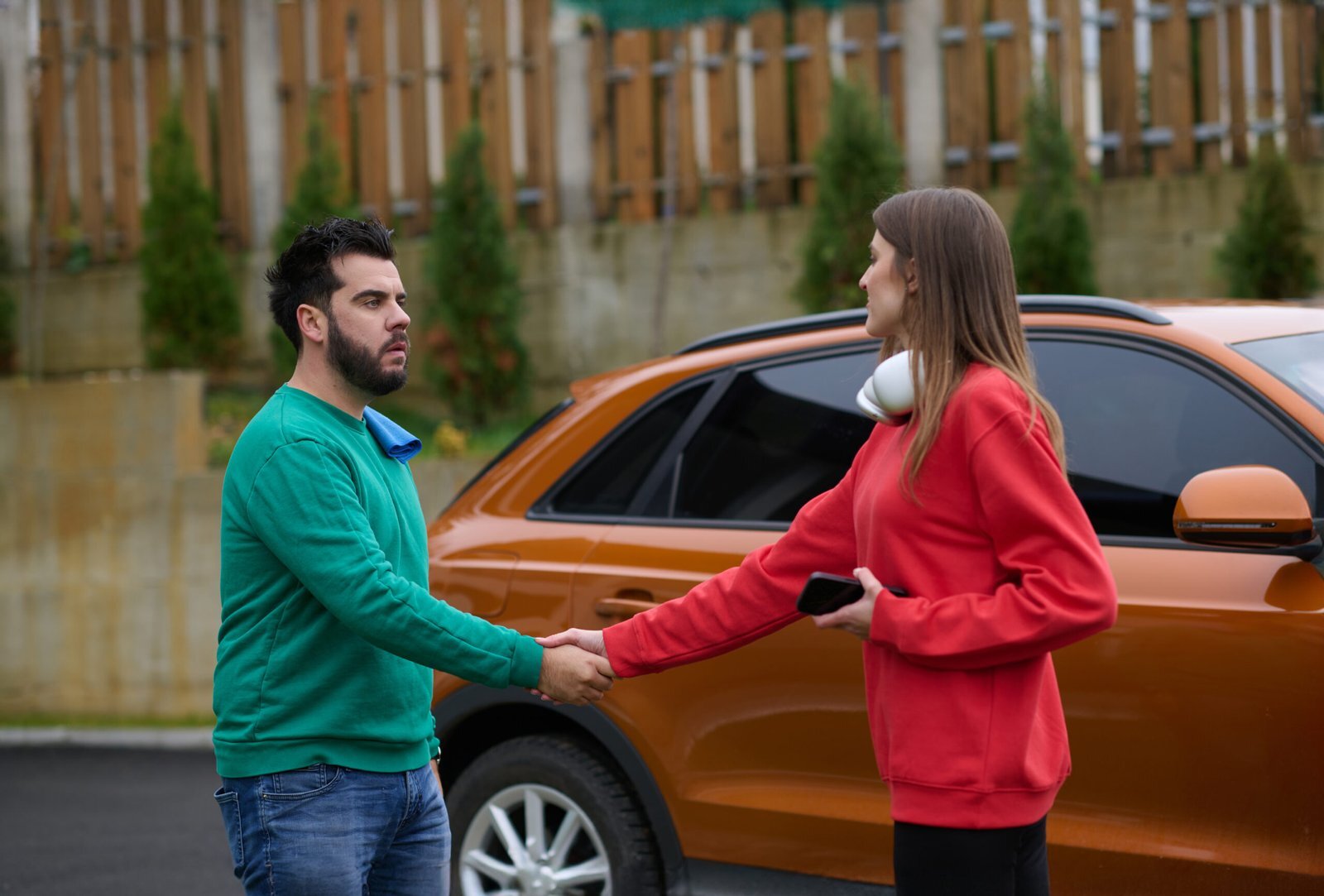 Un homme et une femme se serrant la main devant un véhicule, symbole d’accord ou de résolution de litige.