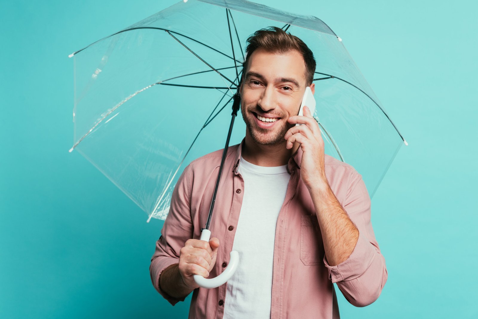 Homme souriant au téléphone sous un parapluie transparent, symbole de protection et d’accompagnement.