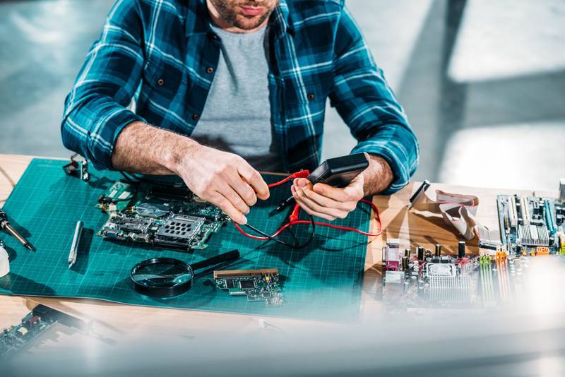 Technicien testant une carte mère avec un multimètre pour diagnostic électronique.